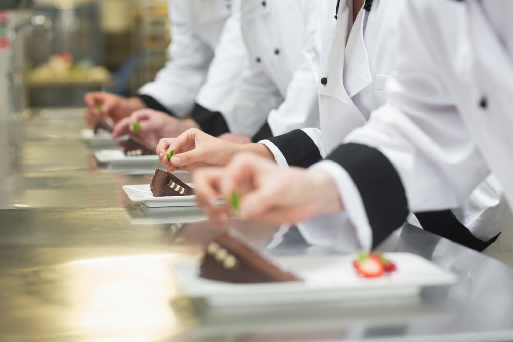 Team of chefs garnishing dessert plates in a busy kitchen